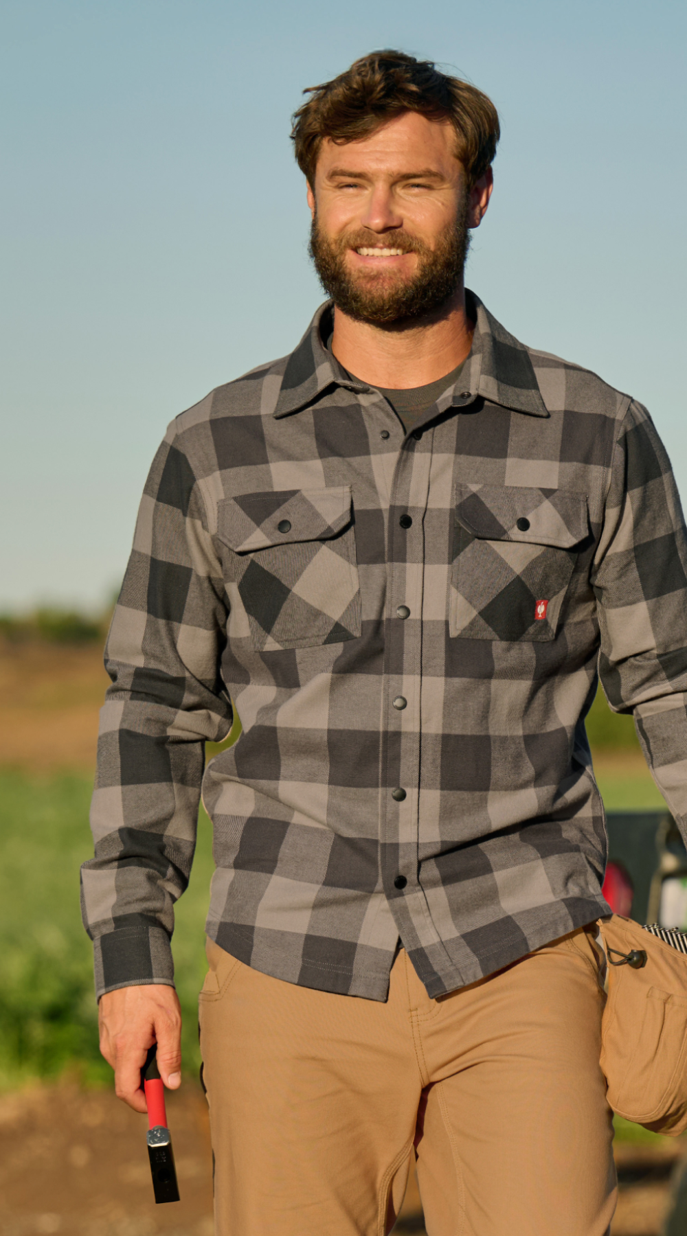 A man walks in a rural area in a grey and black flannel shirt from strauss