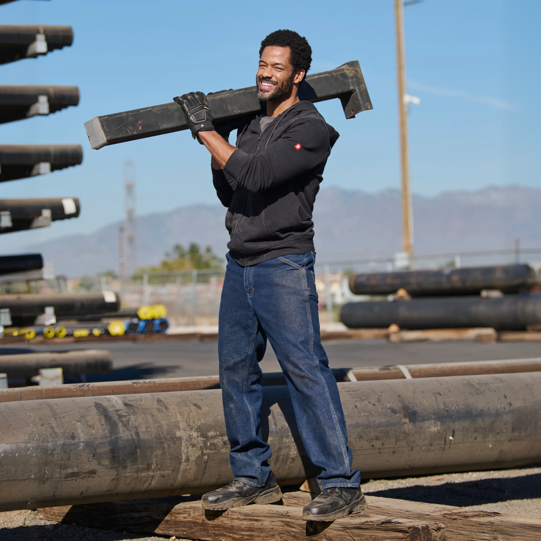 Man carrying a large pipe on his shoulder in an industrial setting