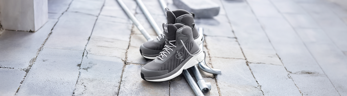 A pair of grey work boots on a concrete floor and metal pipes