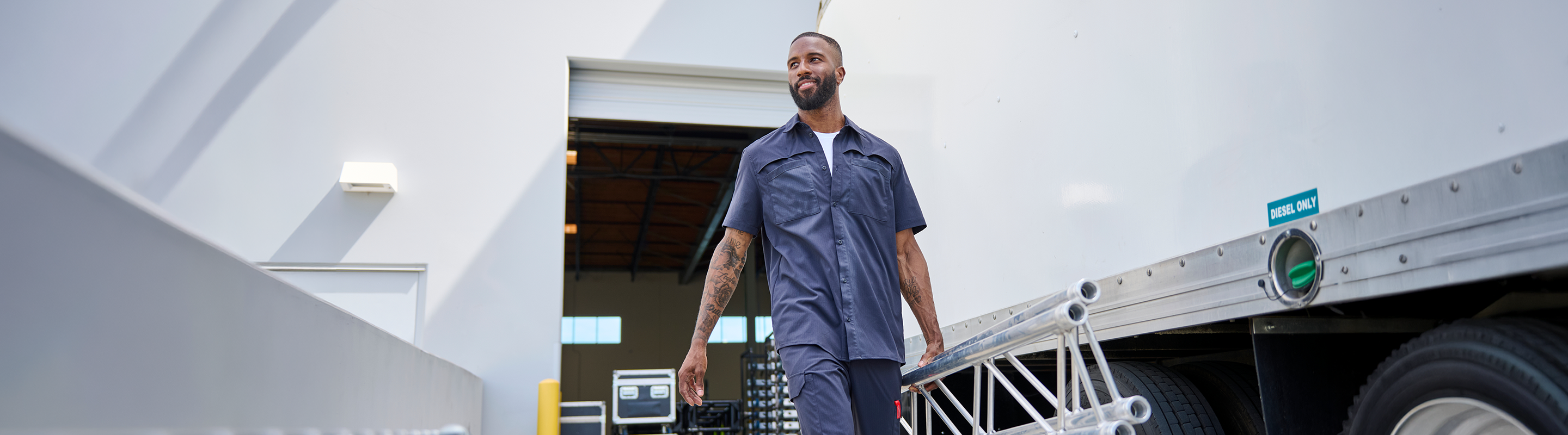 A man in a blue work uniform walks beside a large silver cargo container in a bright industrial setting.