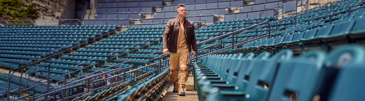 Nick Swisher walking through the stands of a baseball stadium wearing beige and brown STRAUSS workwear