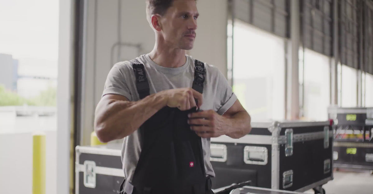 A man stands at a loading dock in e.s.T:aktik Stretch Ripstop work bibs. The camera shows close ups of material details and features.