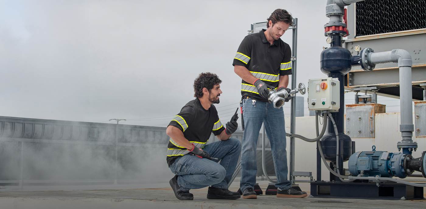 Two workers on a rooftop with industrial equipment in jeans and high vis gear.