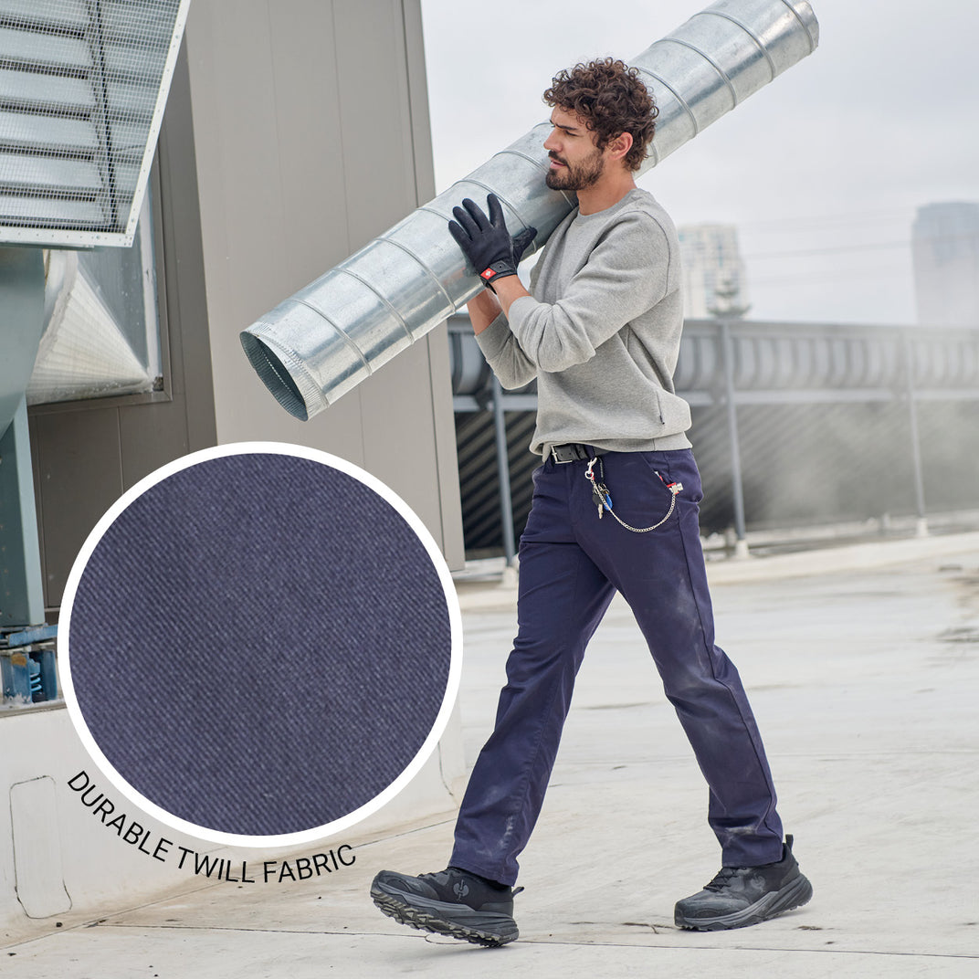 Man carrying a large metal pipe on a rooftop wearing chinos with durable twill fabric highlighted.