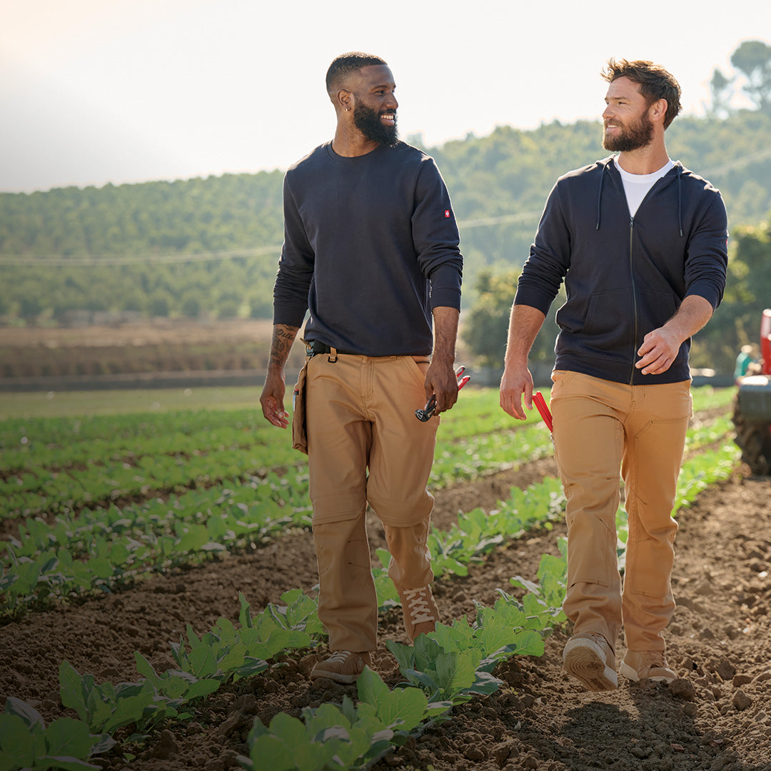 Two farmers walk in a field in STRAUSS workwear made with U.S. Cotton.