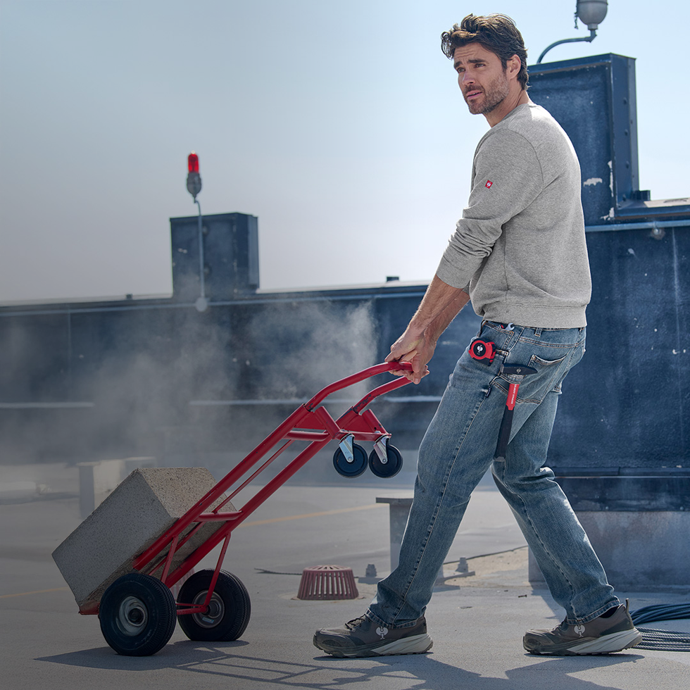 Person using a red hand truck on a rooftop with satellite equipment in the background in Power Denim.