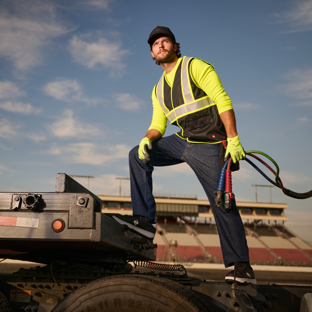 Man in high-visibility clothing standing on a truck with a blue sky background