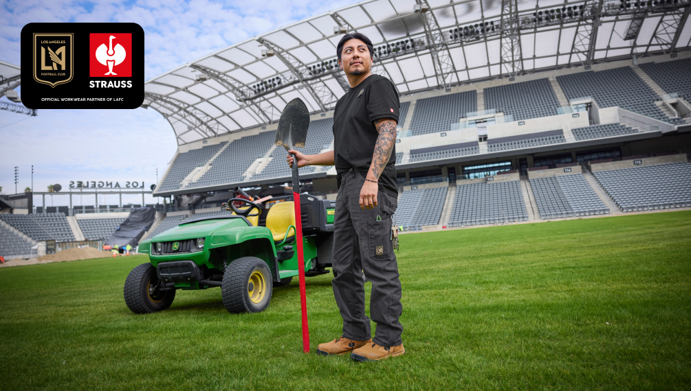A man holding a shovel in his hand, standing in the middle of a soccer pitch