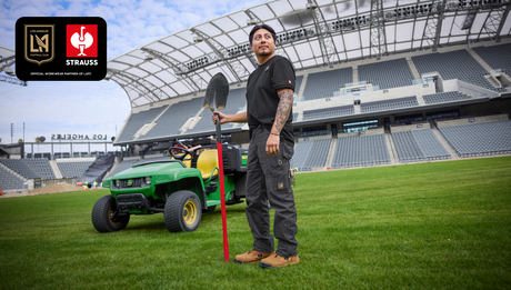 A man holding a shovel in his hand, standing in the middle of a soccer pitch