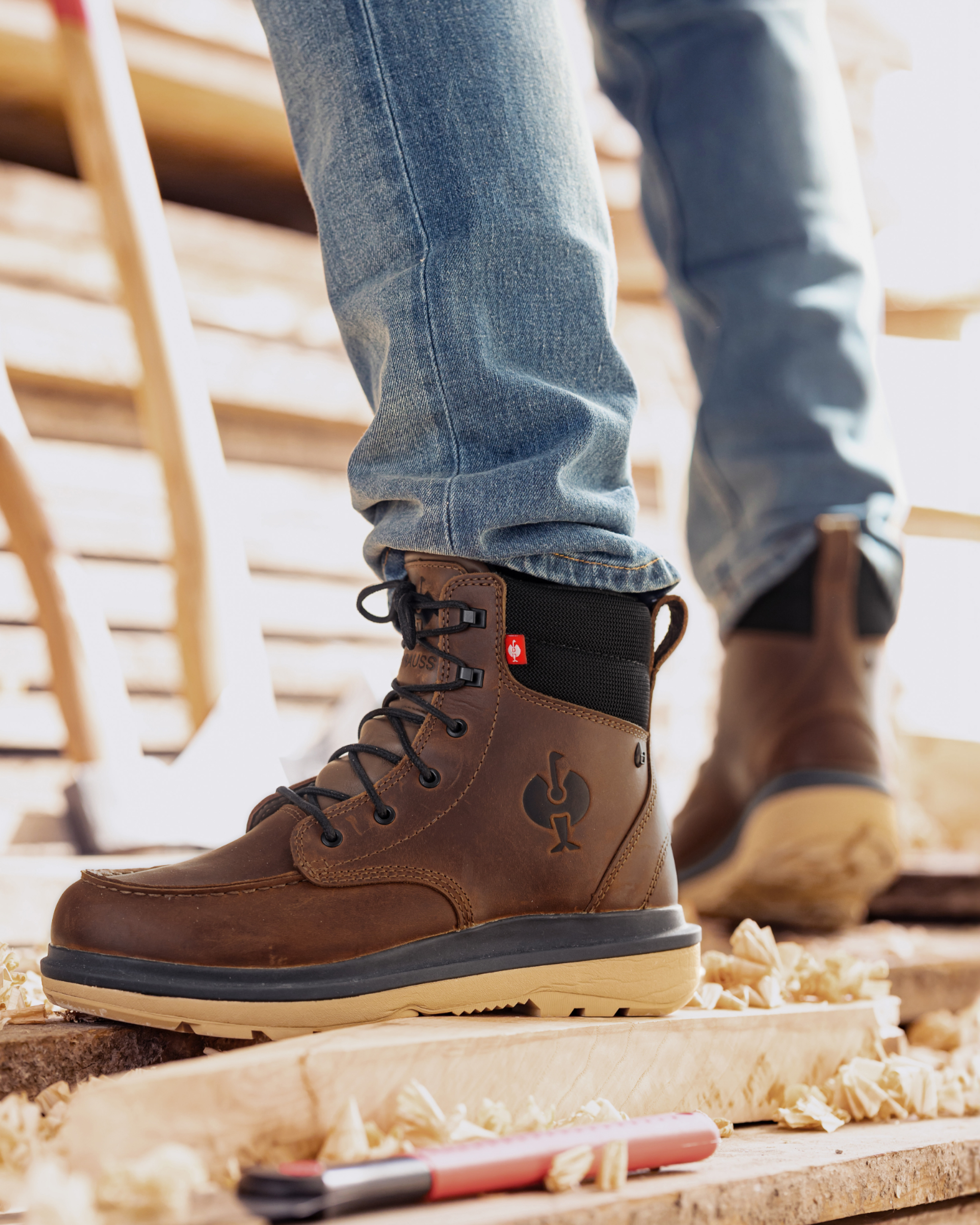 Brown work boots with a visible brand logo worn by a person on a wooden floor.