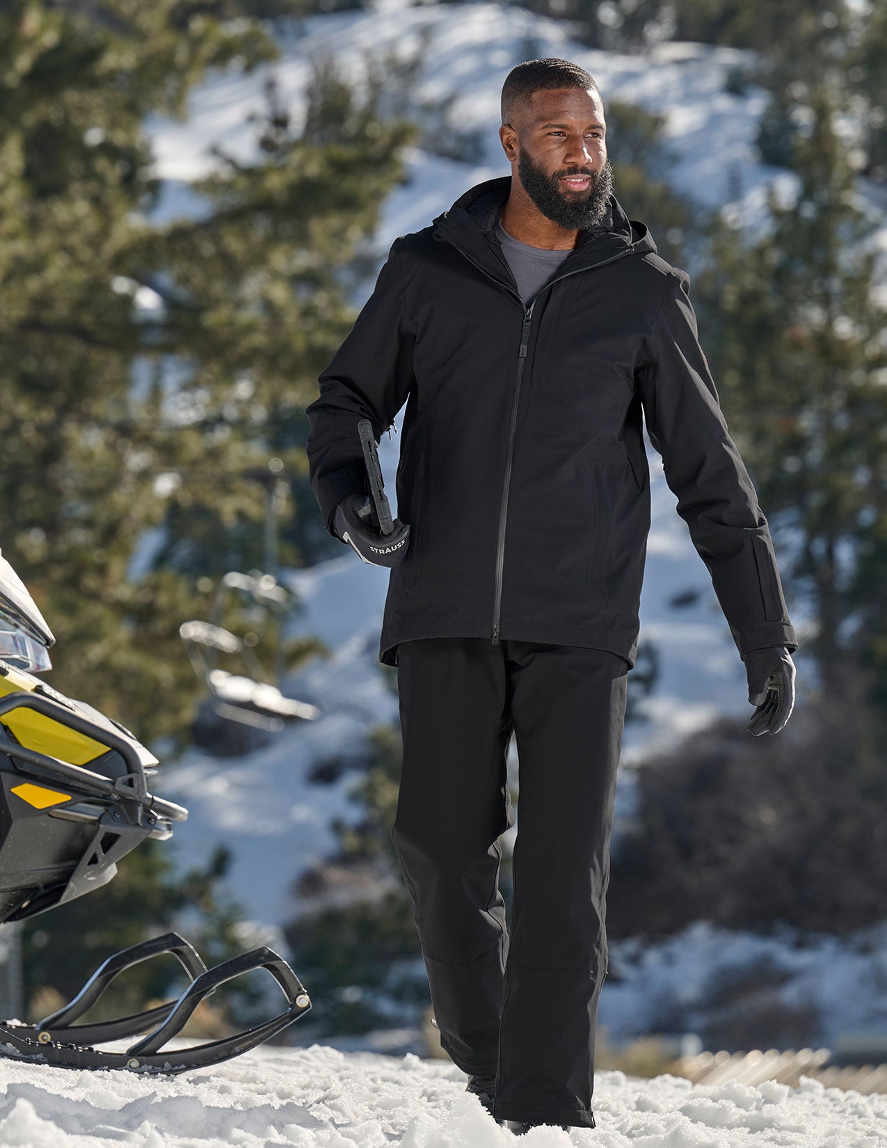 Man in black winter clothing standing in a snowy landscape with trees.