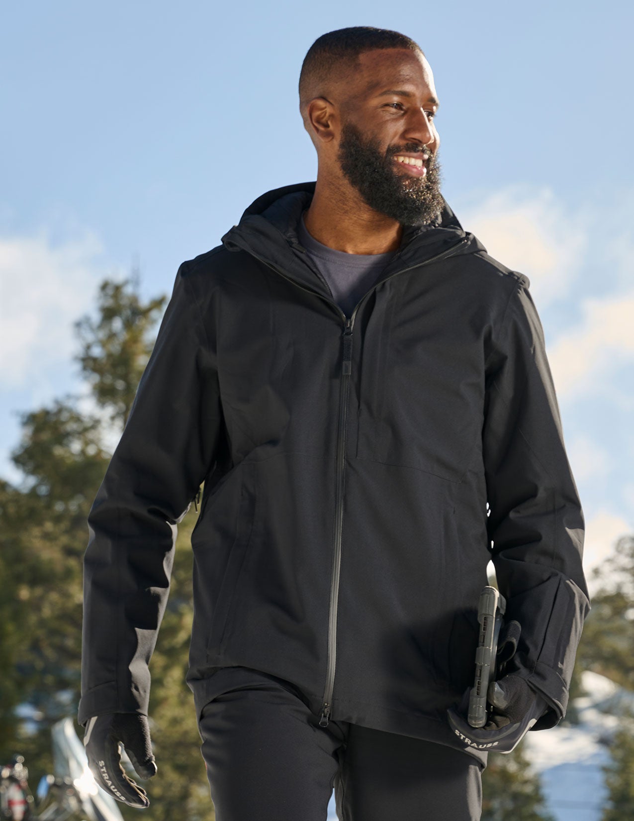 Man wearing a black jacket outdoors with trees and sky in the background.