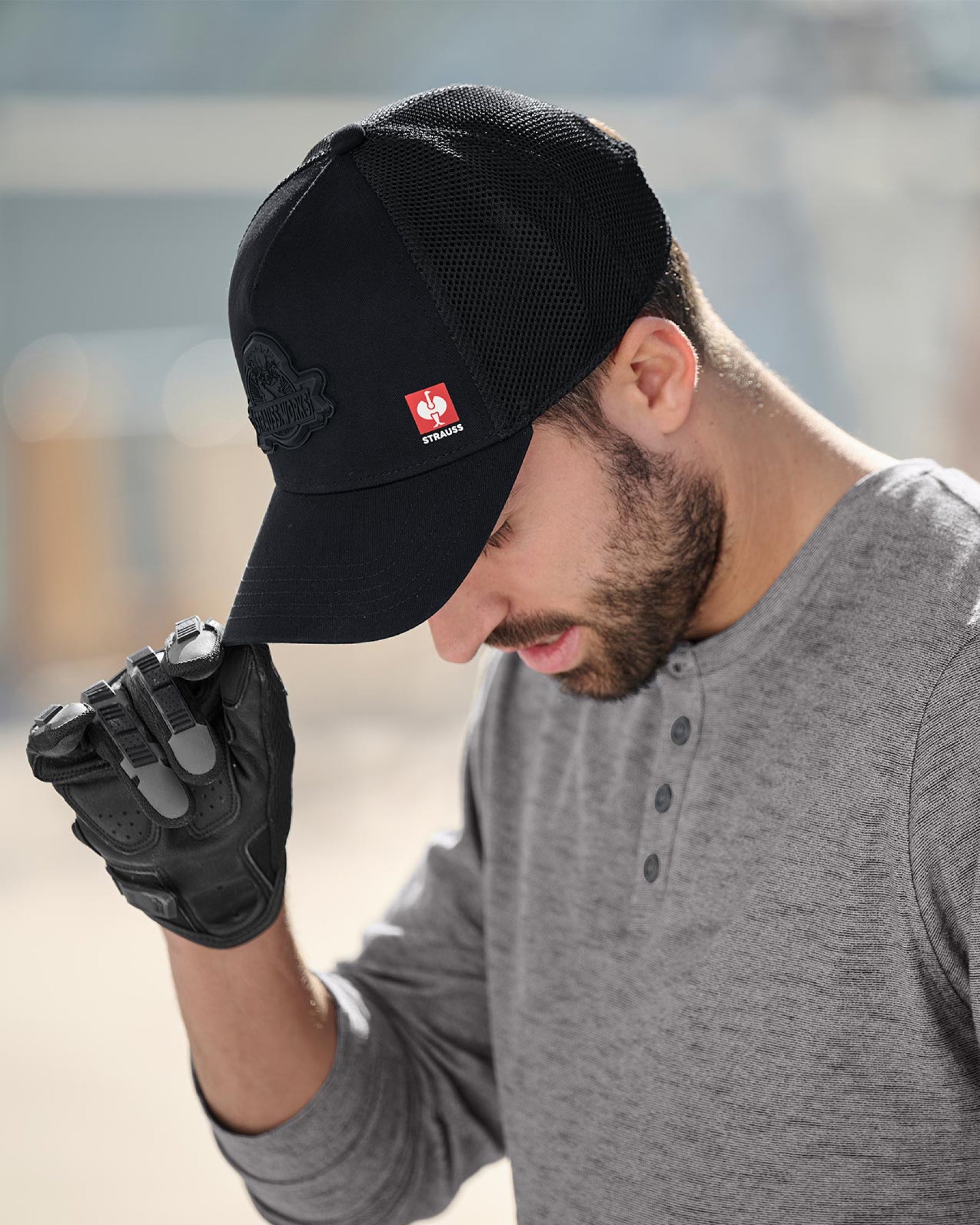 A model wears a black STRAUSS Workwear trucker hat with a casual STRAUSS workwear outfit.
