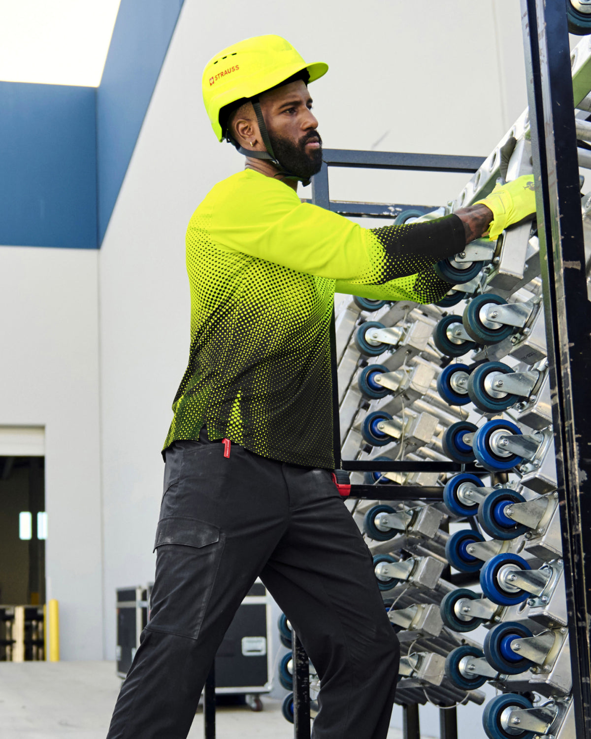A bright yellow STRAUSS Baseball Style Hard Hat with a visor on a model working in a wheel factory.