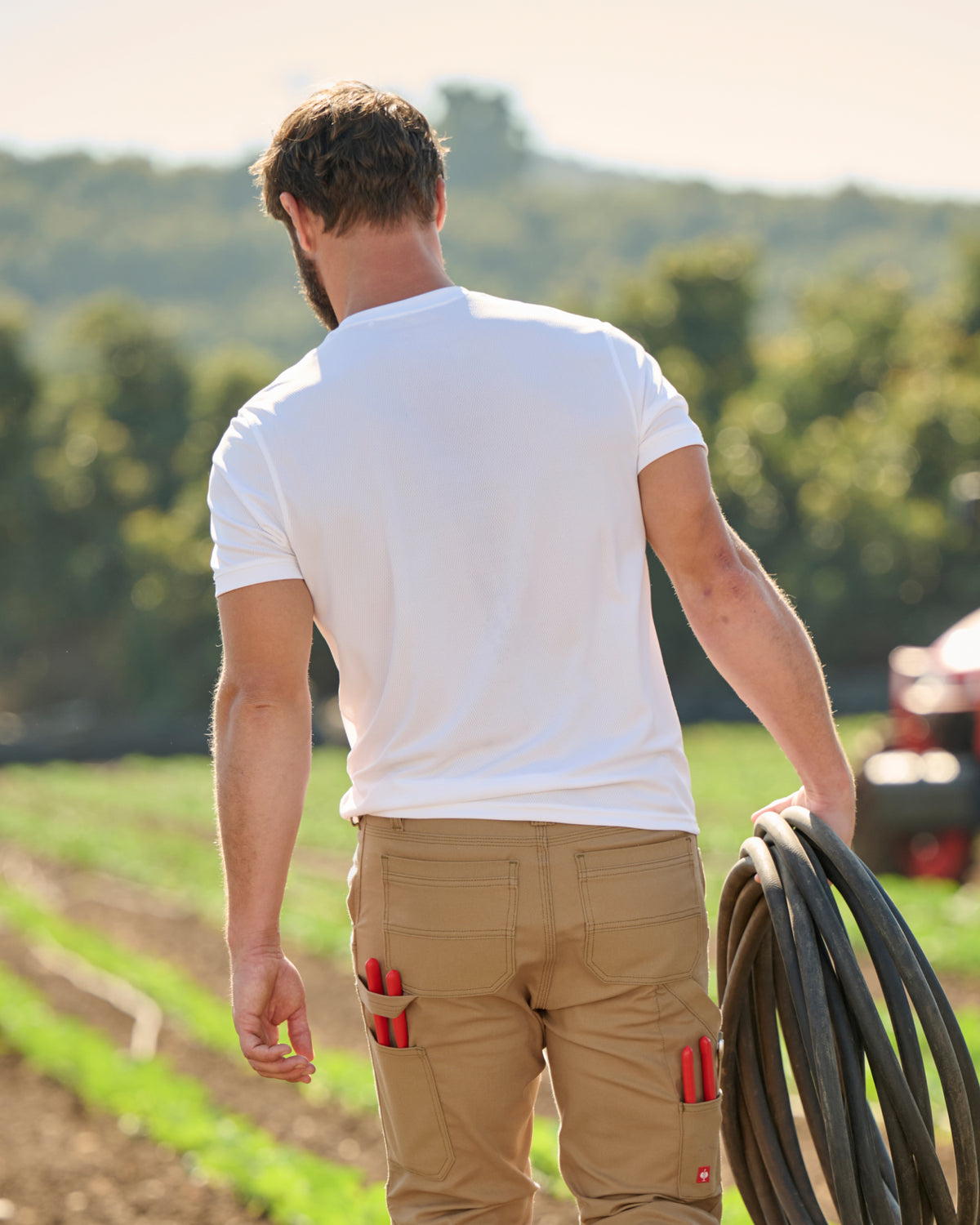 A worker wears the STRAUSS Performance T-Shirt in white with tan work pants beside jobsite equipment