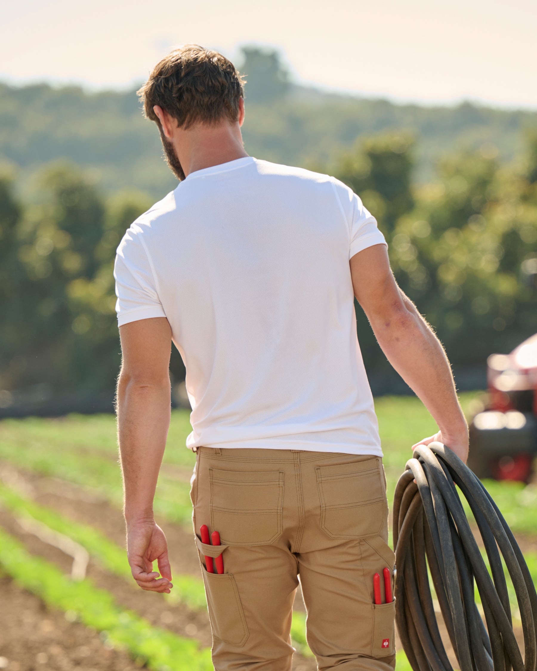 A worker wears the STRAUSS Performance T-Shirt in white with tan work pants beside jobsite equipment