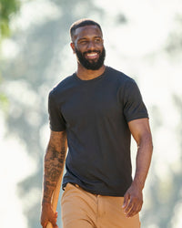 A worker wears the STRAUSS Performance T-Shirt in black with tan work pants on a sunny jobsite