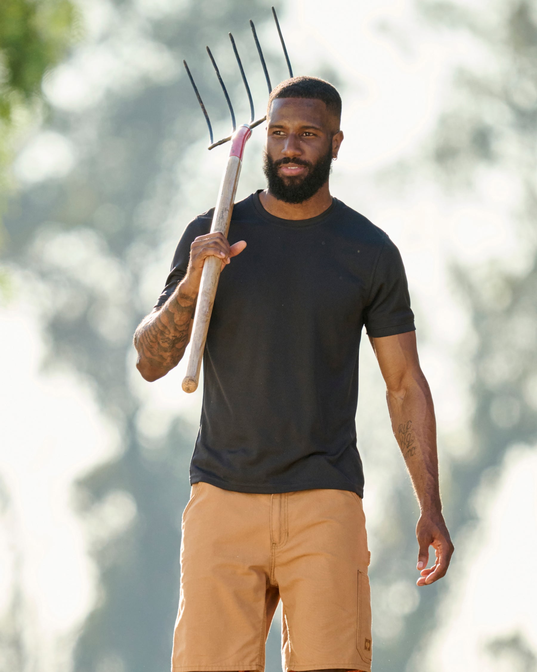 A worker wears the STRAUSS Performance T-Shirt in black with tan work pants while working in a field