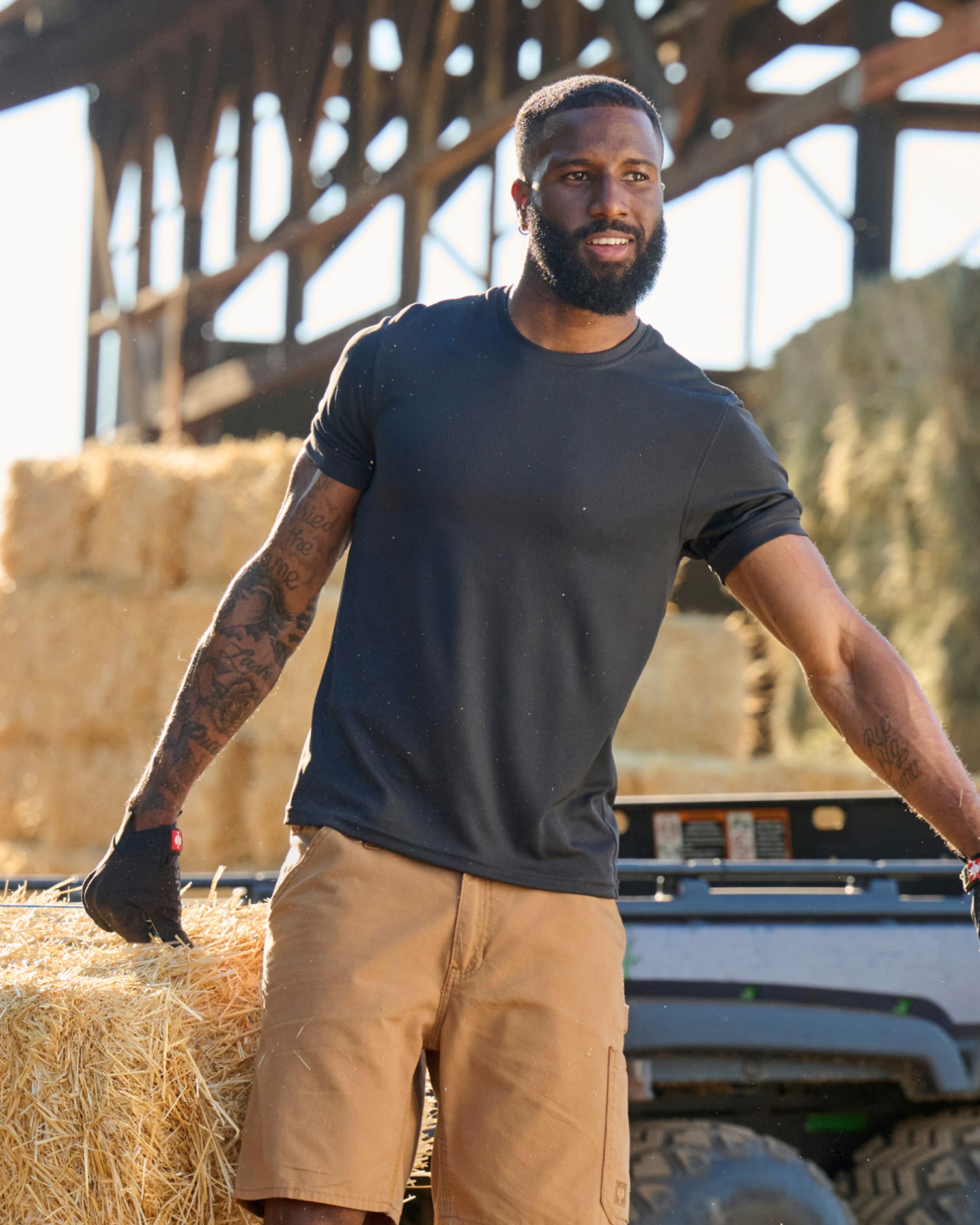 A worker wears the STRAUSS Performance T-Shirt in black with tan work pants beside jobsite equipment
