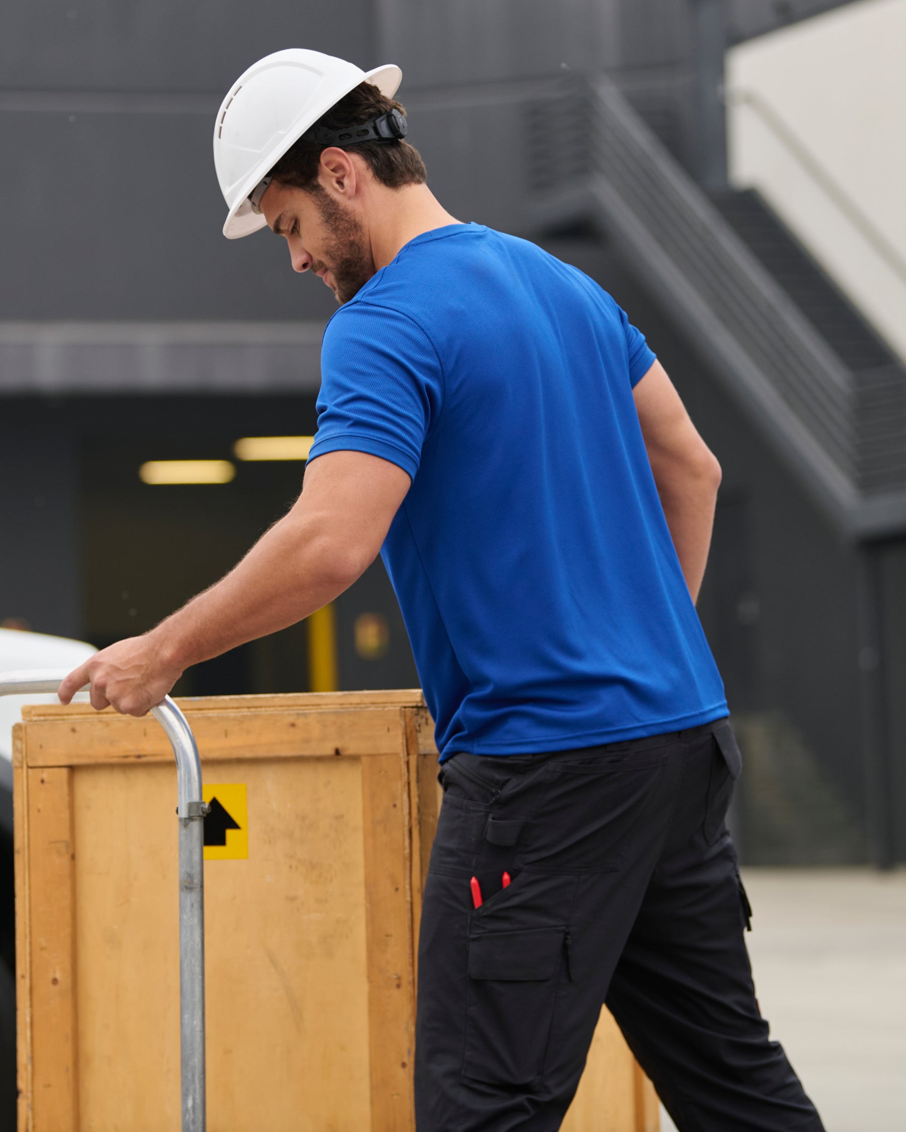 A worker wears the STRAUSS Performance T-Shirt in royal blue beside jobsite equipment