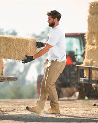 A worker wears the STRAUSS Performance Polo Shirt in white with tan work pants while working in a field