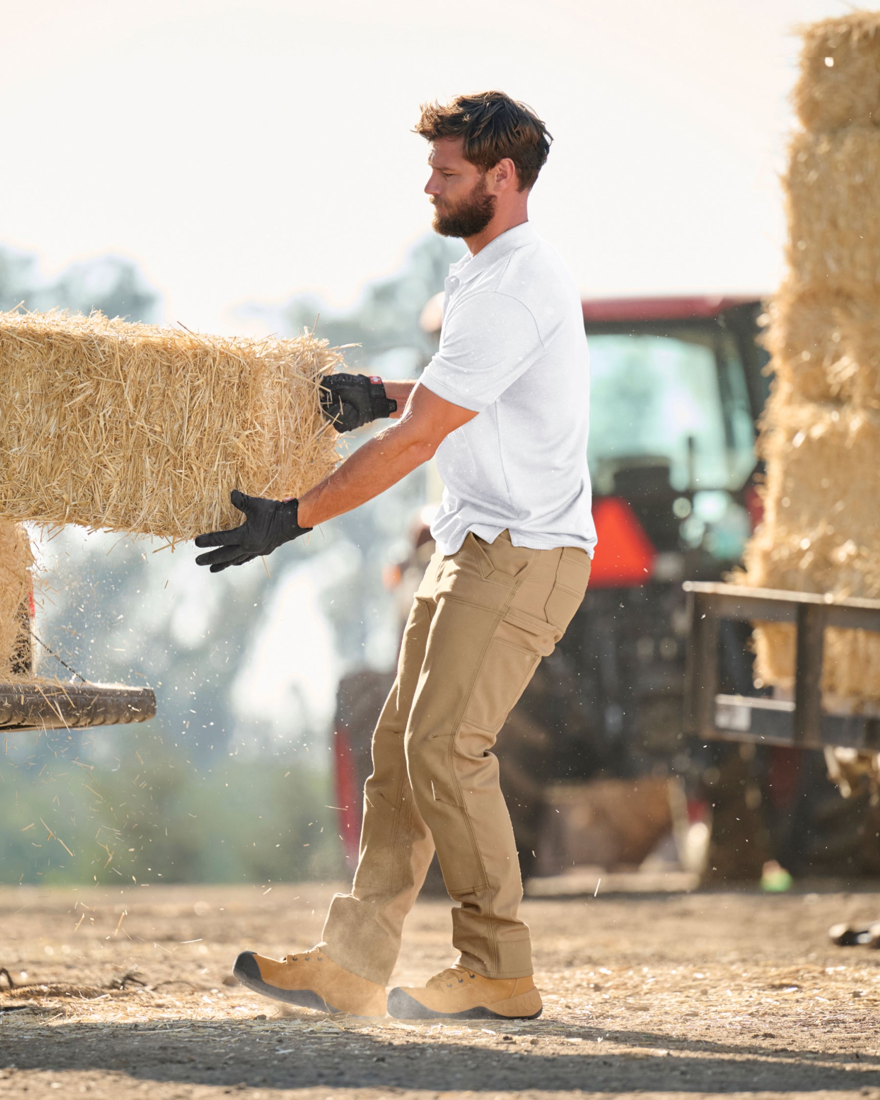 A worker wears the STRAUSS Performance Polo Shirt in white with tan work pants while working in a field