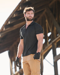 A worker wears the STRAUSS Performance Polo Shirt in black with tan work pants on a sunny jobsite