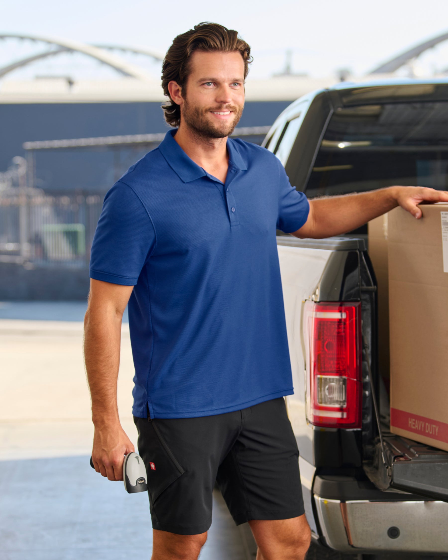 A worker wears the STRAUSS Performance Polo Shirt in royal blue on a sunny jobsite