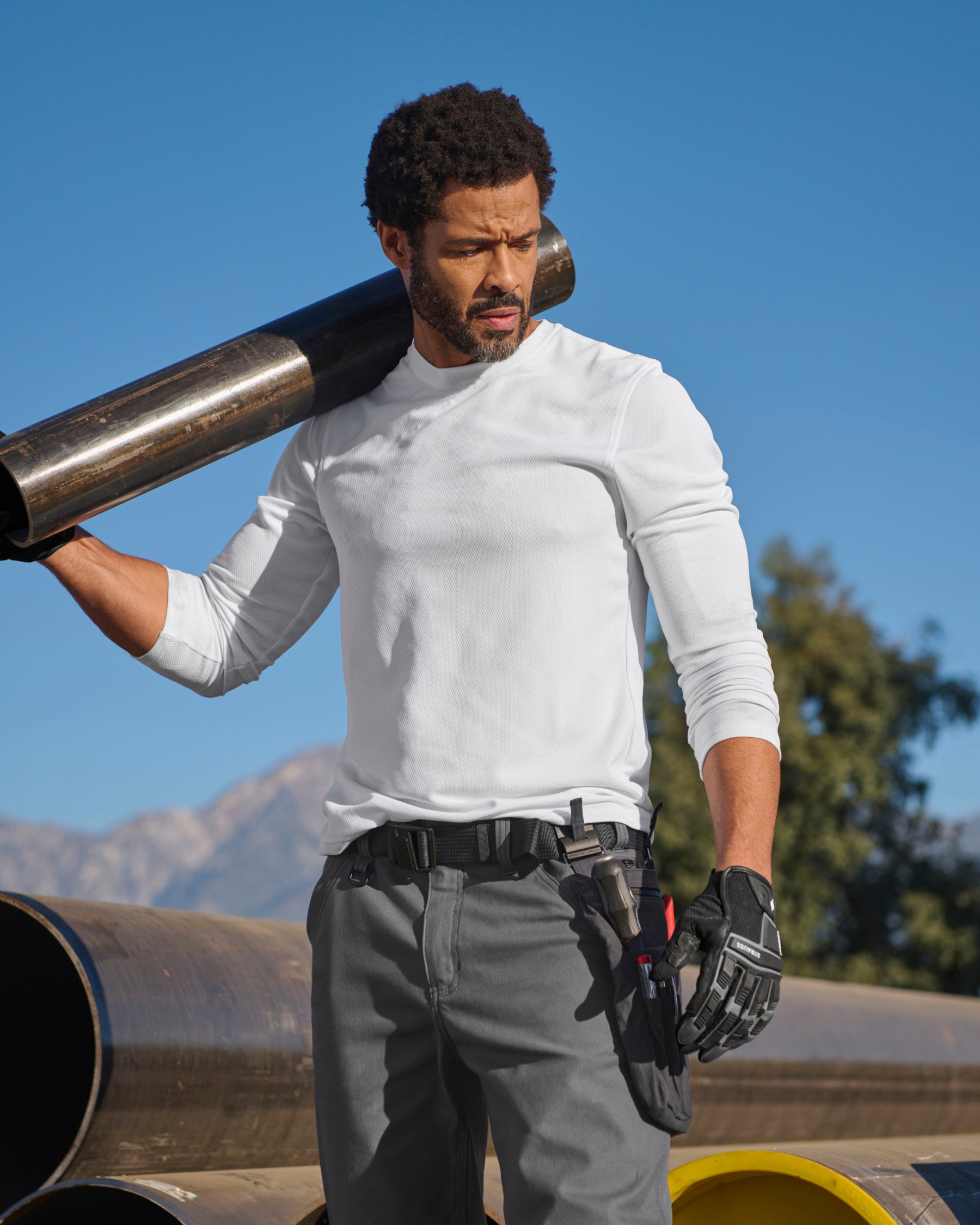 A worker wears the STRAUSS Performance Long Sleeve Shirt in white with tan work pants on a sunny jobsite