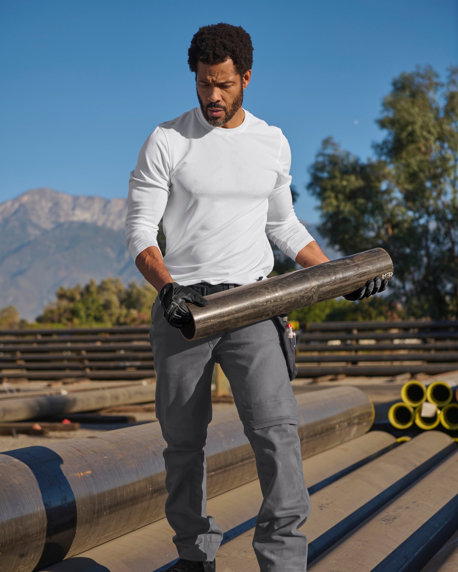 A worker wears the STRAUSS Performance Long Sleeve Shirt in white with tan work pants while working in a field