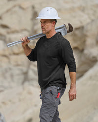 A worker wears the STRAUSS Performance Long Sleeve Shirt in black with tan work pants on a sunny jobsite