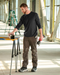 A worker wears the STRAUSS Performance Long Sleeve Shirt in black with tan work pants beside jobsite equipment