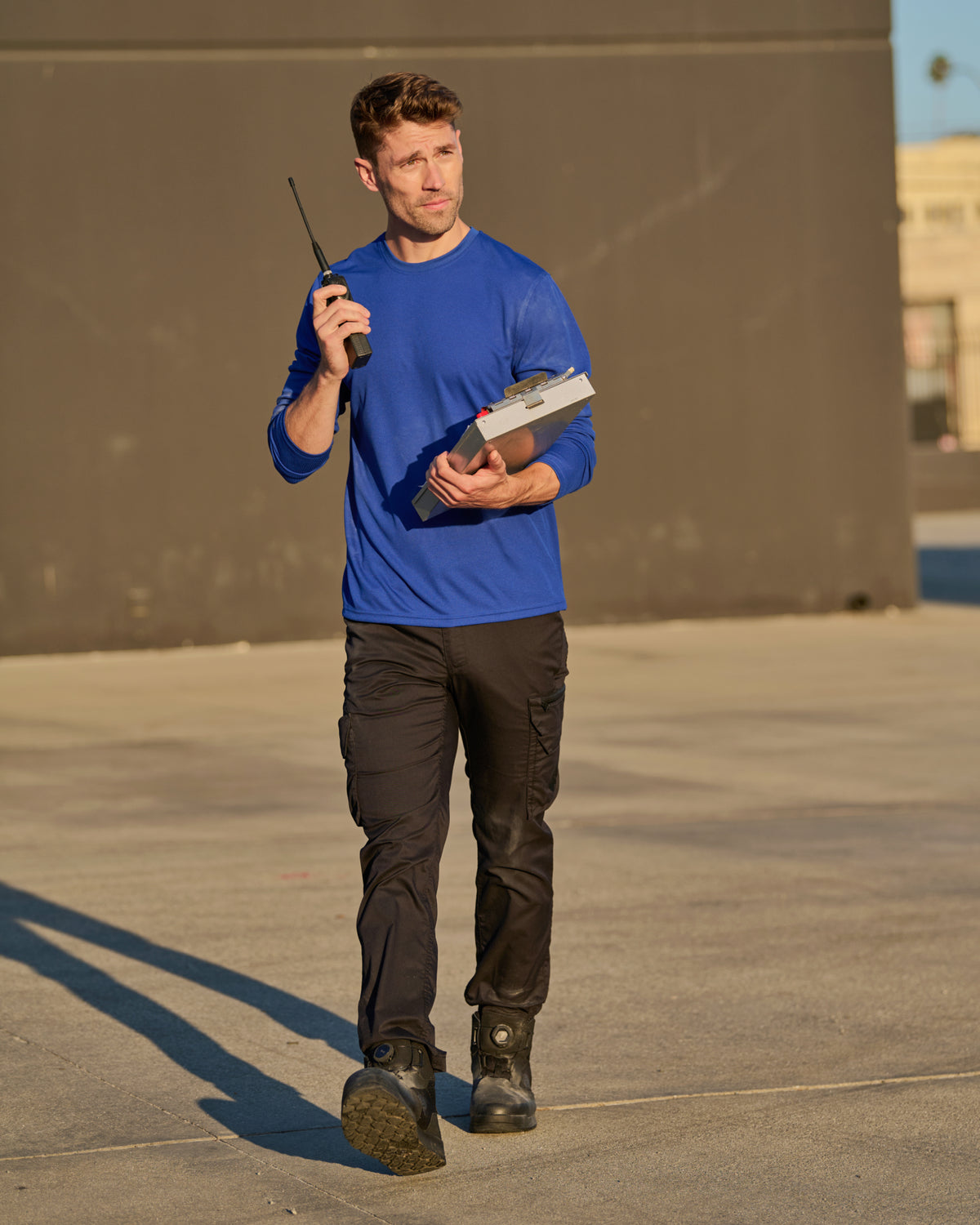 A worker wears the STRAUSS Performance Long Sleeve Shirt in royal blue with tan work pants while working in a field