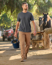 A worker wears the STRAUSS Performance T-Shirt in carbon gray with tan work pants while working in a field