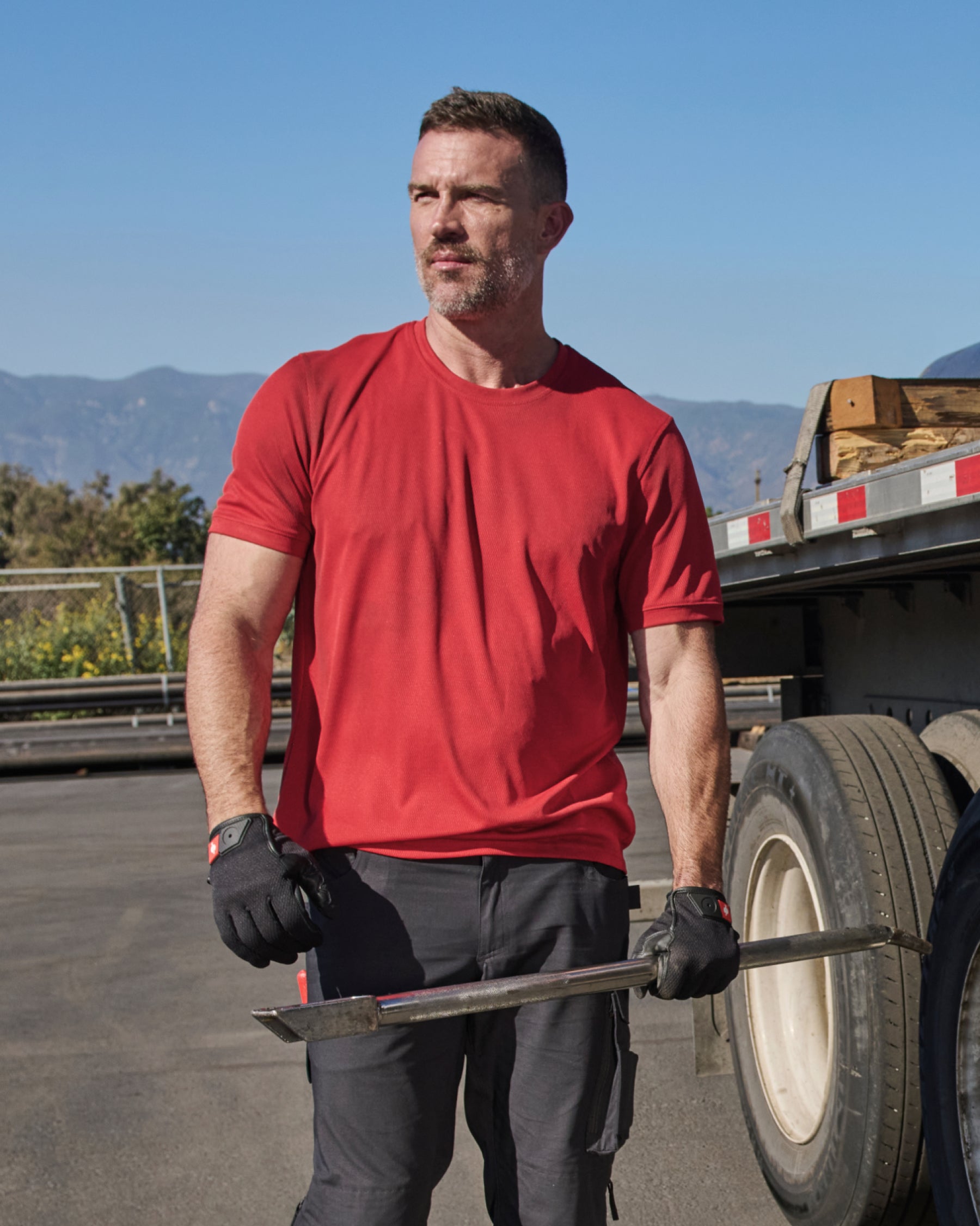 A worker wears the STRAUSS Performance T-Shirt in fire red on a sunny jobsite