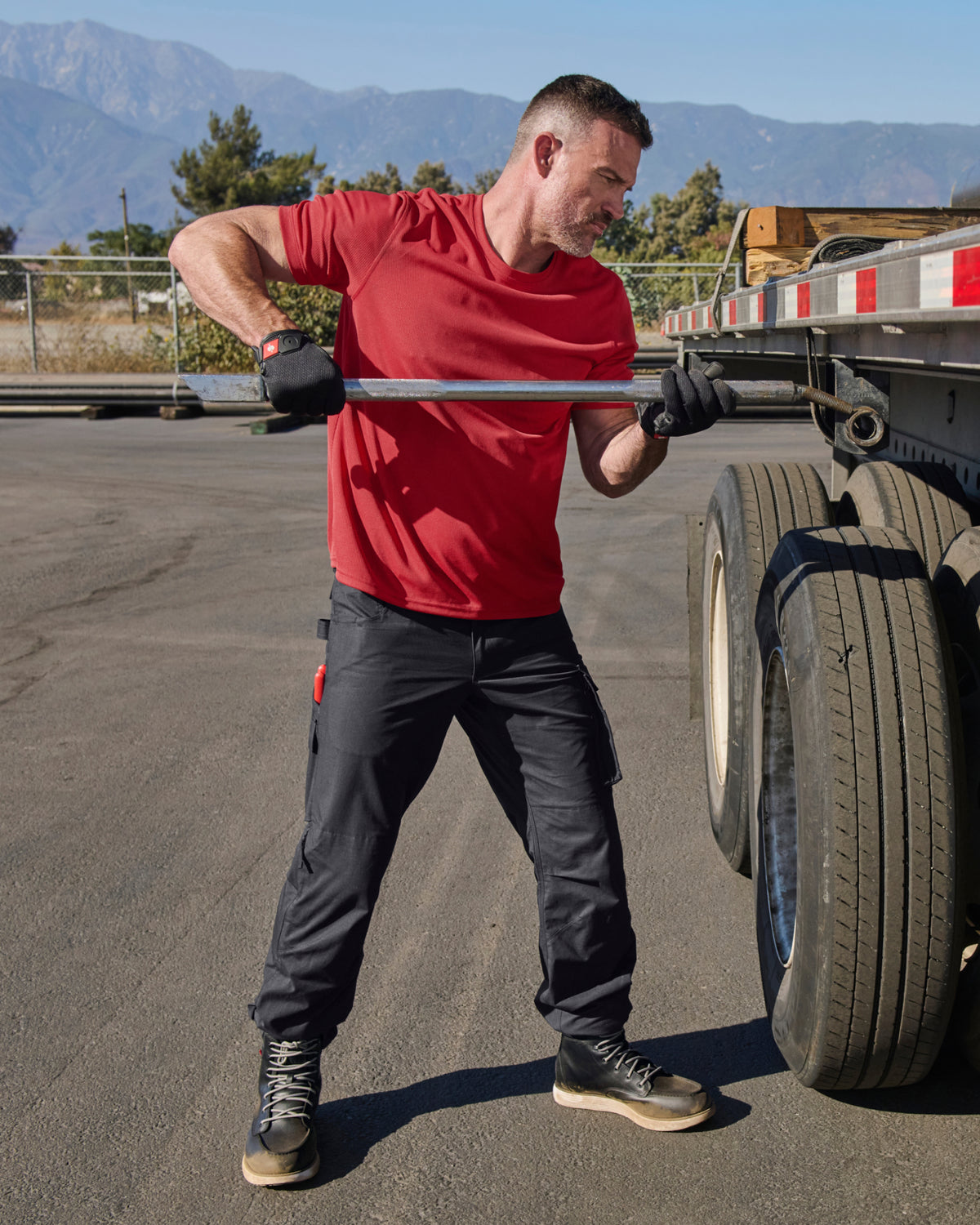 A worker wears the STRAUSS Performance T-Shirt in fire red with tan work pants while working in a field