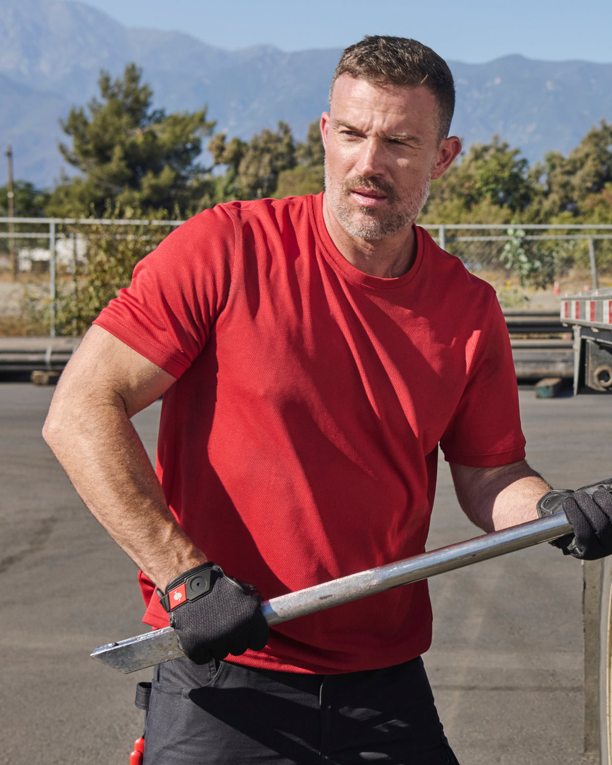 A worker wears the STRAUSS Performance T-Shirt in fire red beside jobsite equipment