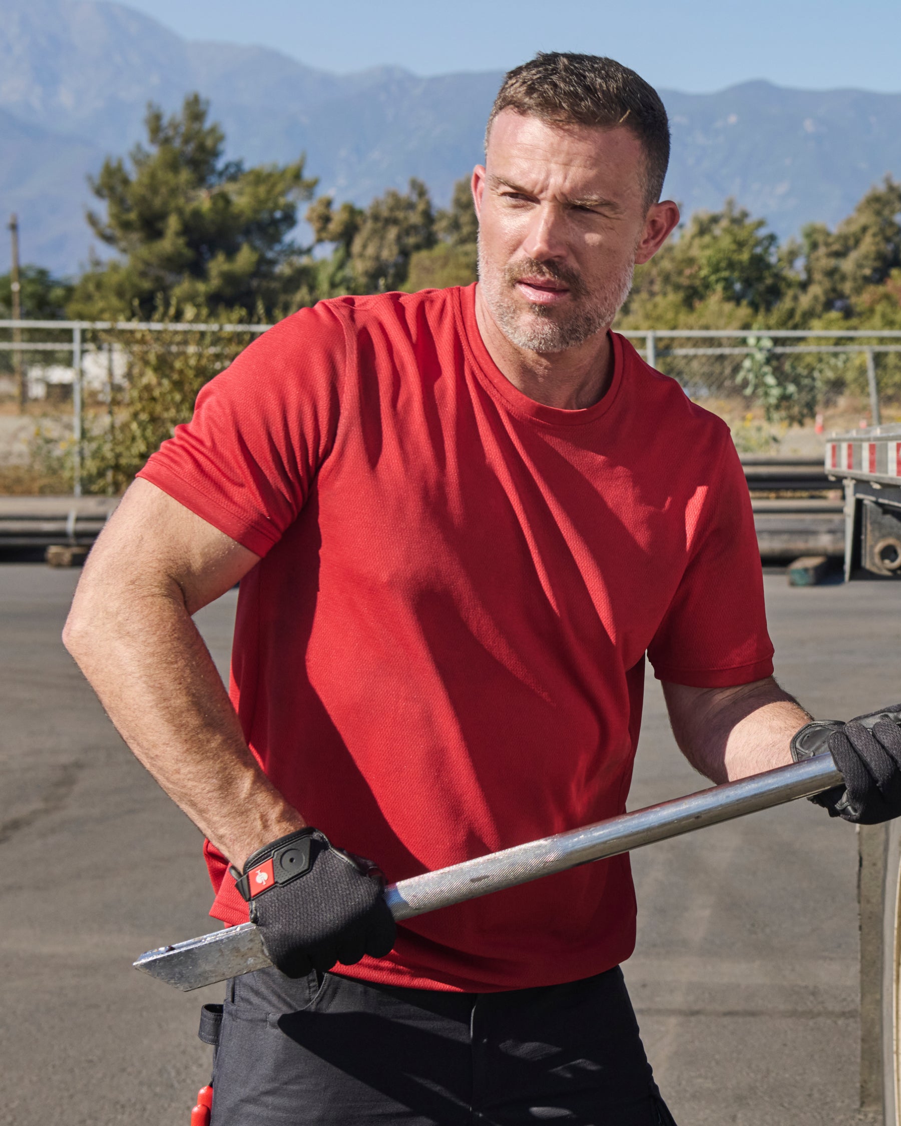 A worker wears the STRAUSS Performance T-Shirt in fire red beside jobsite equipment