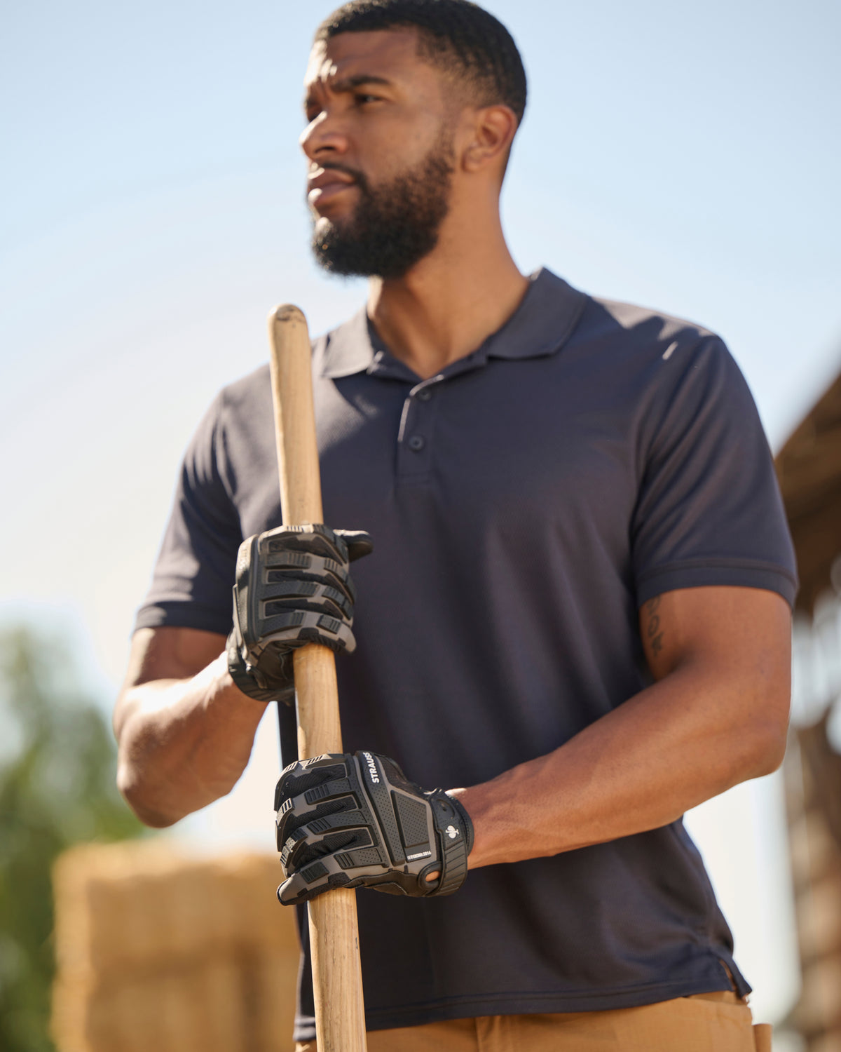 A worker wears the STRAUSS Performance Polo Shirt in nero blue with tan work pants on a sunny jobsite