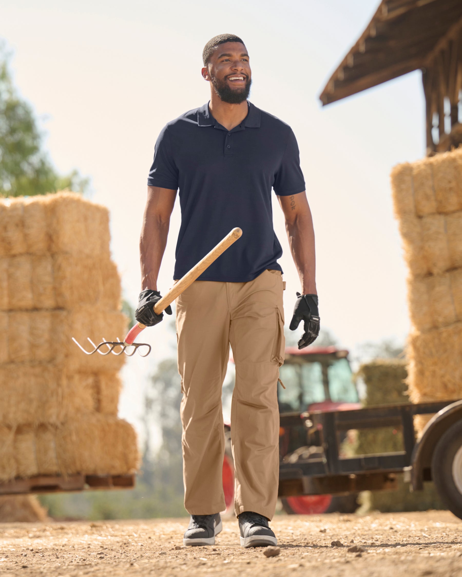 A worker wears the STRAUSS Performance Polo Shirt in nero blue with tan work pants while working in a field