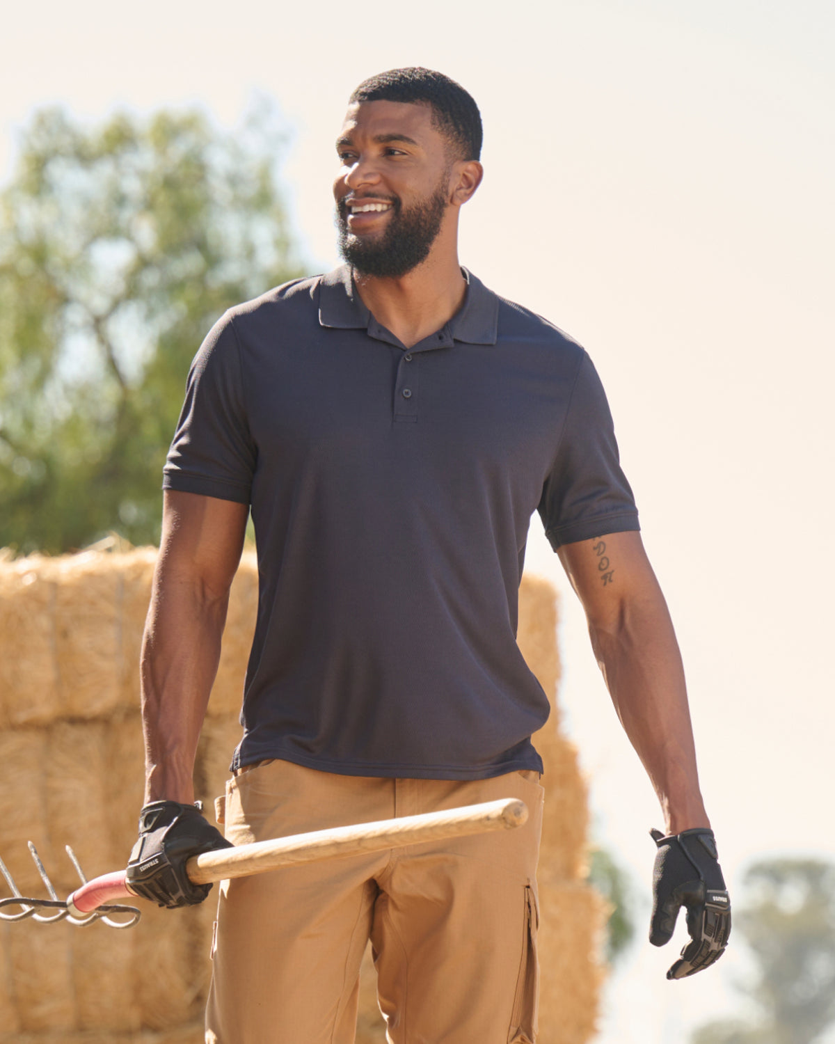 A worker wears the STRAUSS Performance Polo Shirt in nero blue with tan work pants beside jobsite equipment