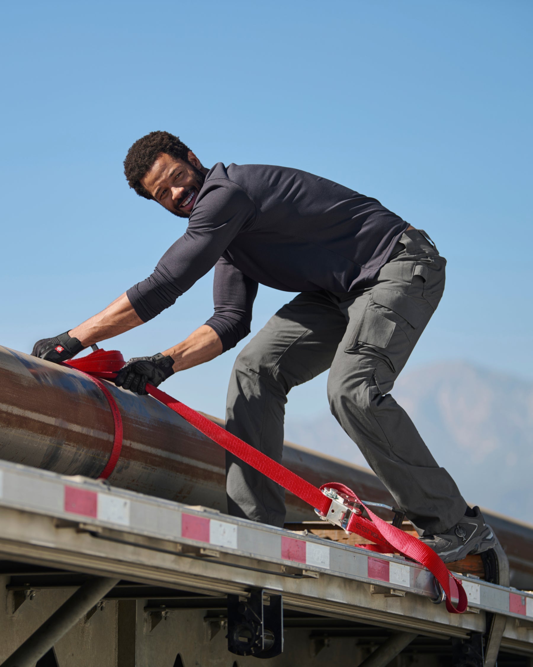 A worker wears the STRAUSS Performance Long Sleeve Shirt in nero blue with tan work pants while working on a roof