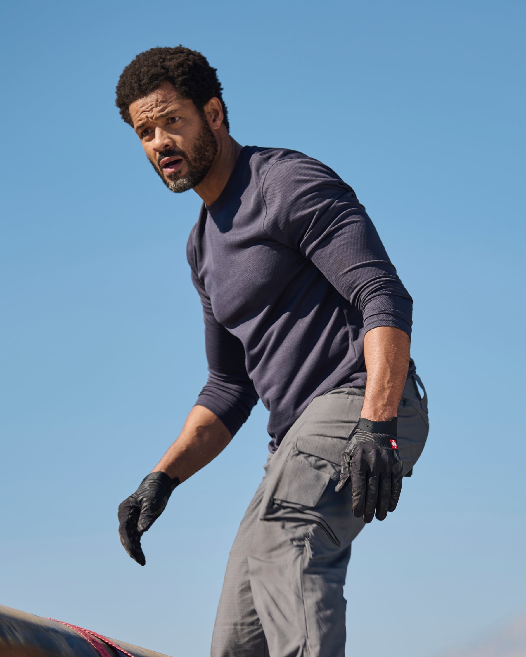 A worker wears the STRAUSS Performance Long Sleeve Shirt in nero blue with tan work pants on a roof