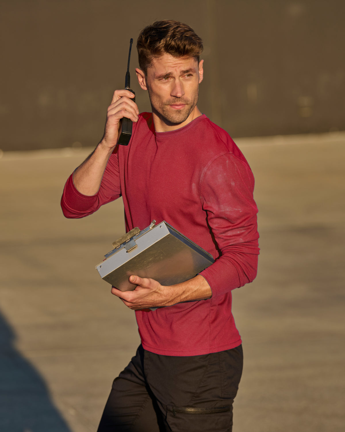 A worker wears the STRAUSS Performance Long Sleeve Shirt in fire red with tan work pants on a sunny jobsite