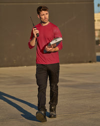 A worker wears the STRAUSS Performance Long Sleeve Shirt in fire red with tan work pants