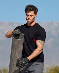 A worker wears the STRAUSS Pocket T-Shirt e.s.iconic in black with cargo work pants on a gravel jobsite