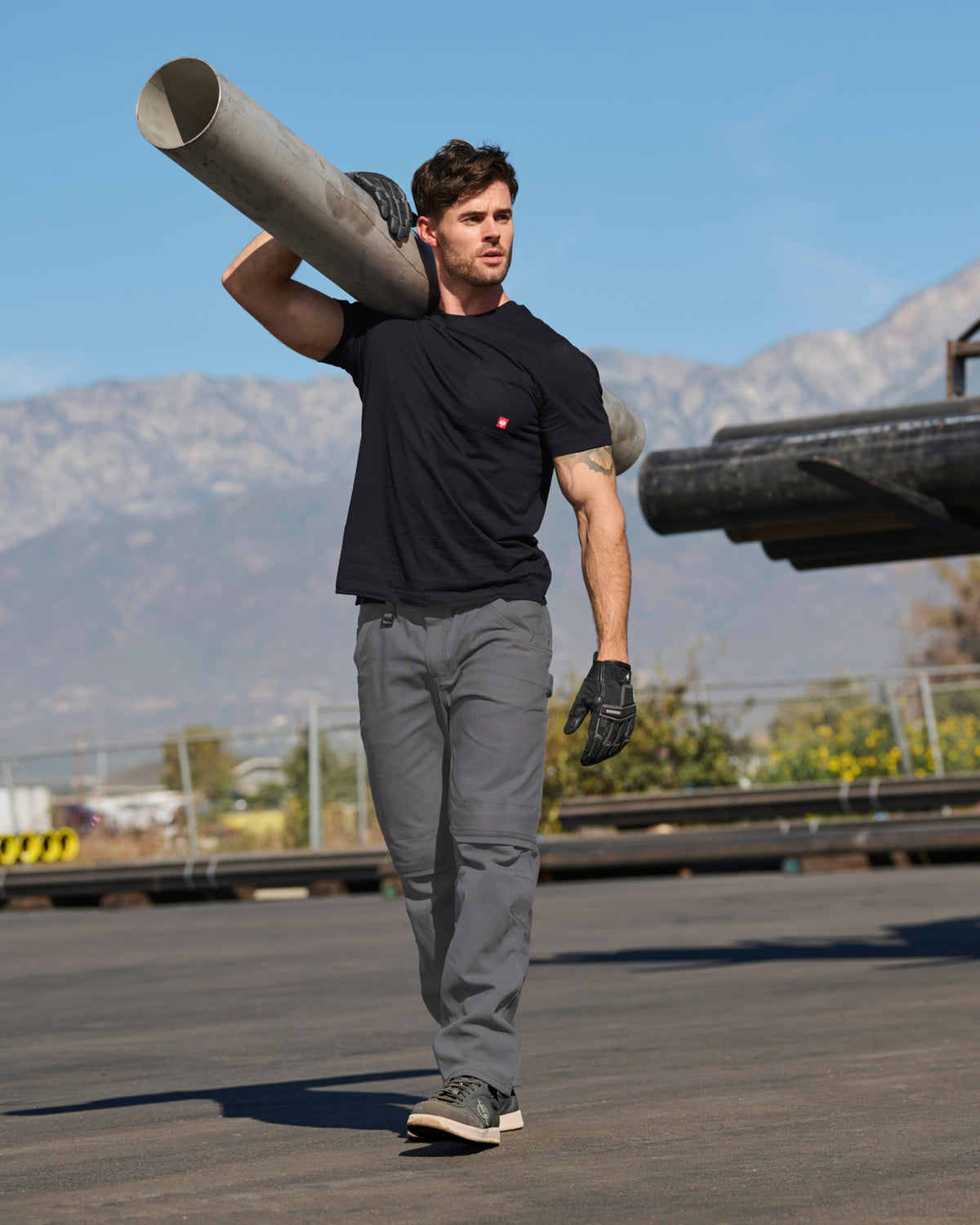 A worker wears the STRAUSS Pocket T-Shirt e.s.iconic in black with work pants beside stacked building materials
