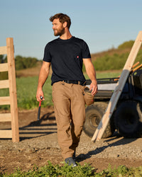 A worker wears the STRAUSS Pocket T-Shirt e.s.iconic in black with work pants near a workshop doorway