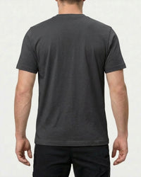 A model wears the STRAUSS Pocket T-Shirt e.s.iconic in carbon gray with work pants and work boots, showing the shirt fit