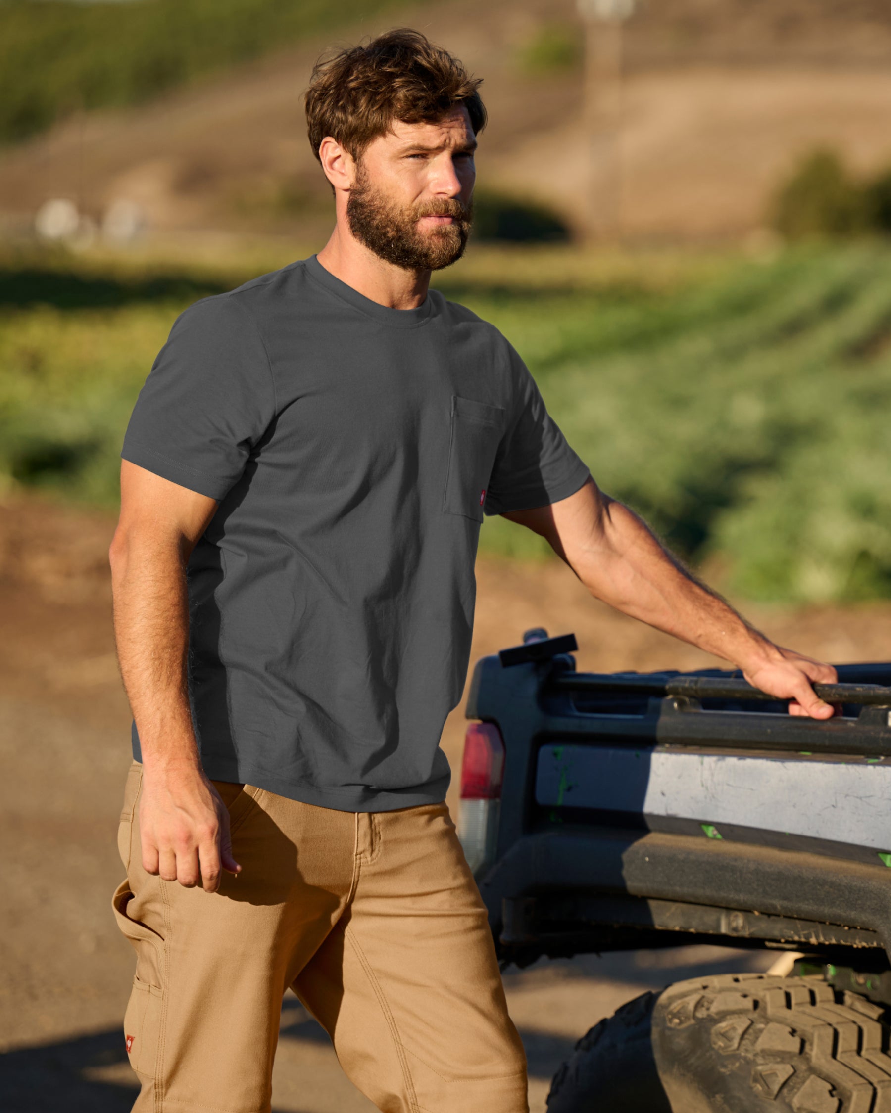 A worker wears the STRAUSS Pocket T-Shirt e.s.iconic in carbon gray with cargo work pants on a gravel jobsite